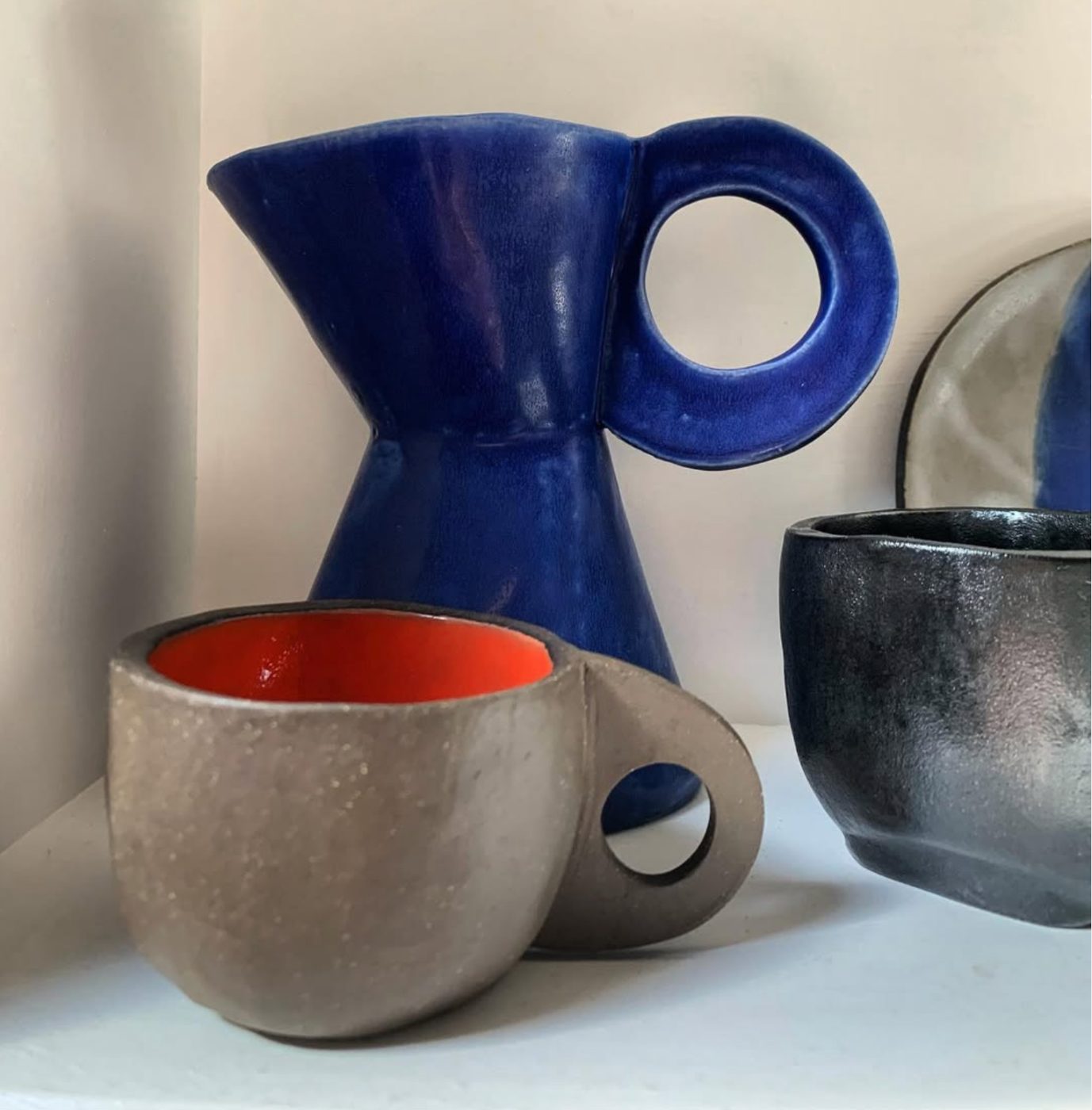 Cobalt pitcher with circle handle beside mug with orange interior