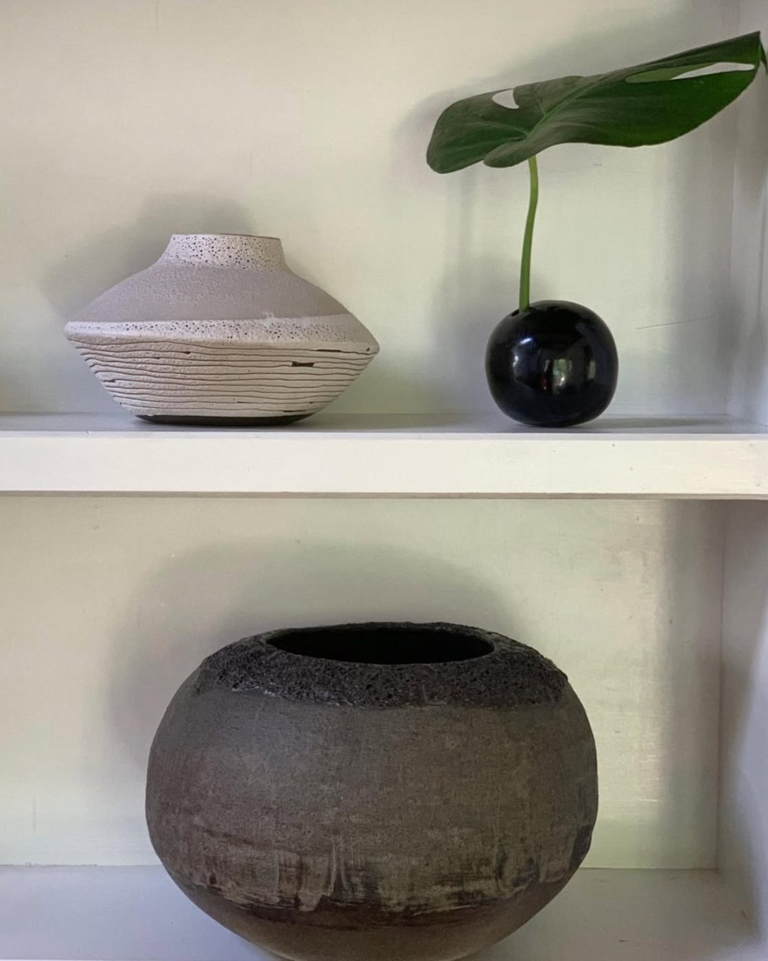Shelf with layered white vase, black sphere and textured pot
